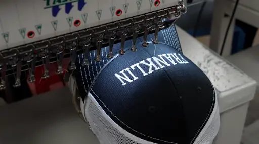 Navy blue hat in embroidery machine with logo being applied