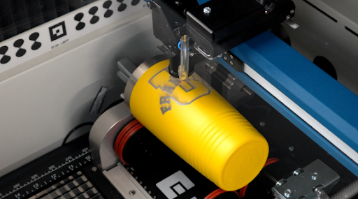 Laser engraving machine producing a design on a yellow drinking cup