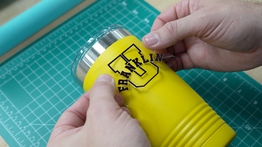 Hands applying UV Direct-to-Film design to a yellow cup